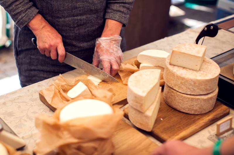 Woman cutting cheese in a fromagerie in Paris